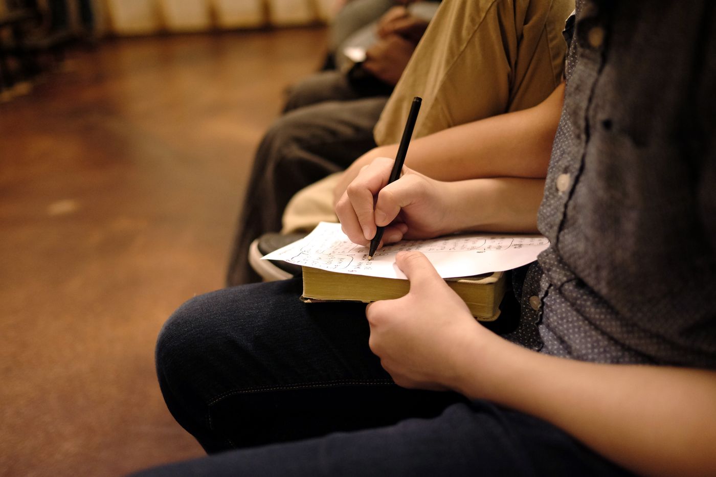 Hands taking notes in a notebook over an open Bible during the service
