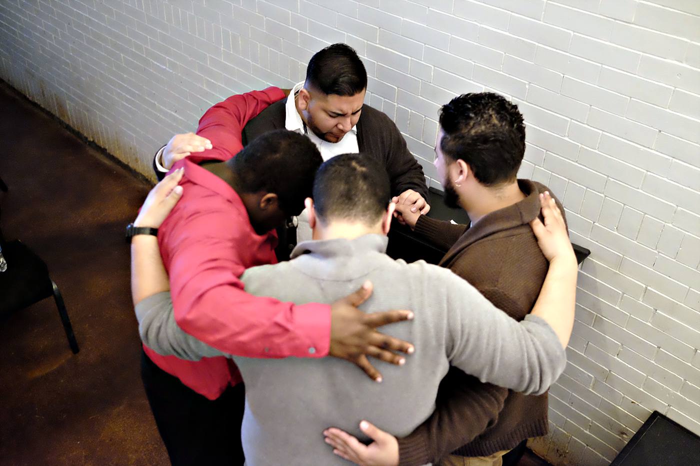Six people standing with their arms around each other, praying